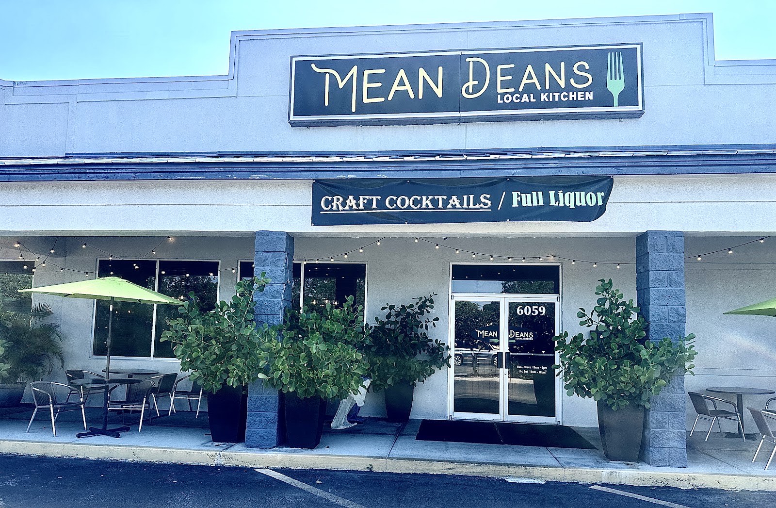 The Mean Deans Local Kitchen storefront with its Art Deco fork sign, Craft Cocktails Full Liquor banner and outdoor patio seating