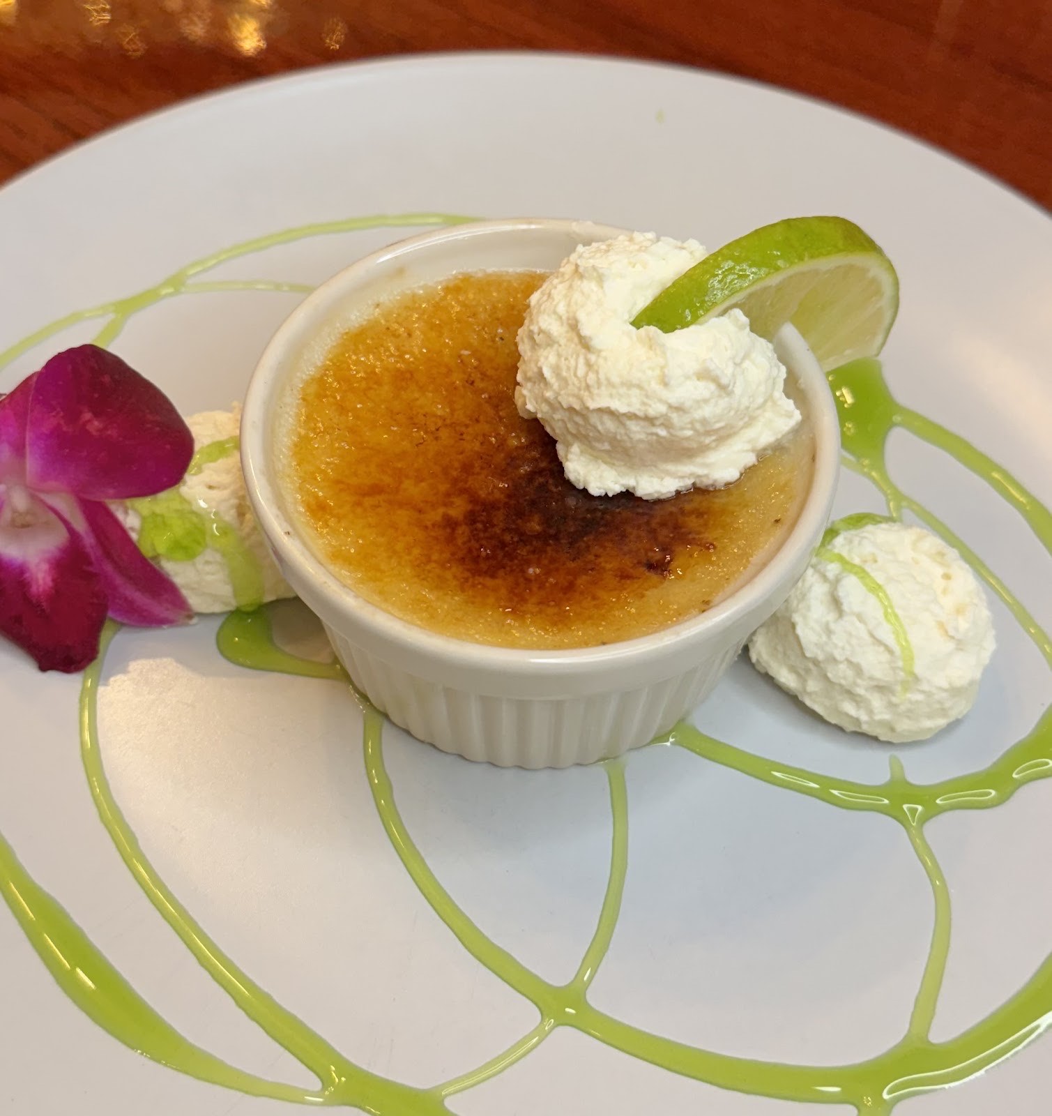 Key lime crème brûlée in a ramekin with a torched sugar top, fresh lime and whipped cream on a lime-painted plate