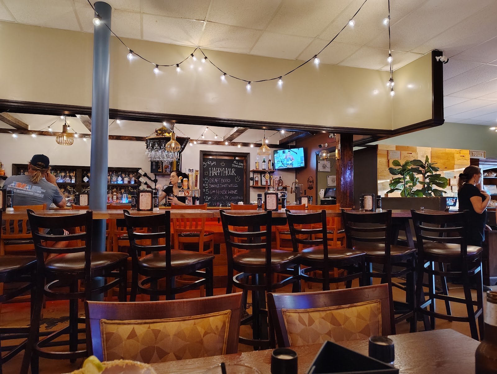The full bar at Mean Deans with hanging glassware, the happy hour chalkboard and string lights